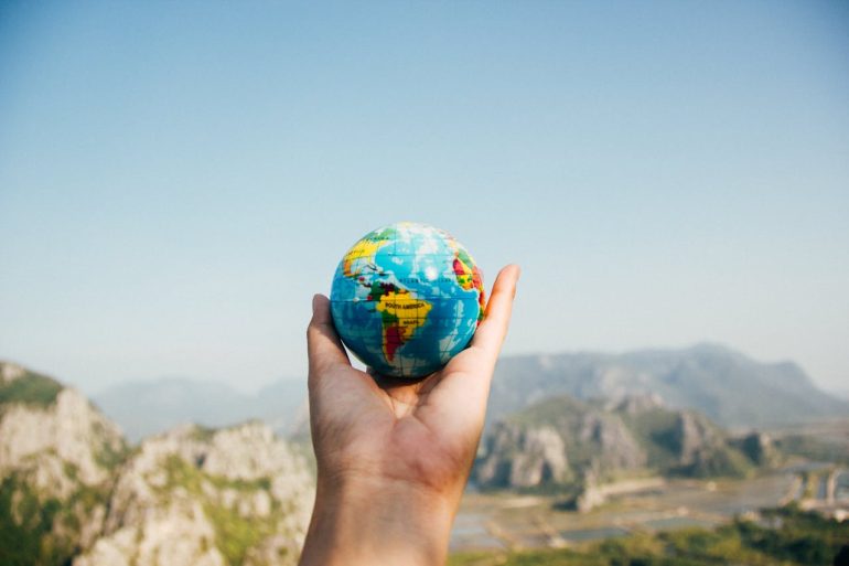 person-holding-world-globe-facing-mountain